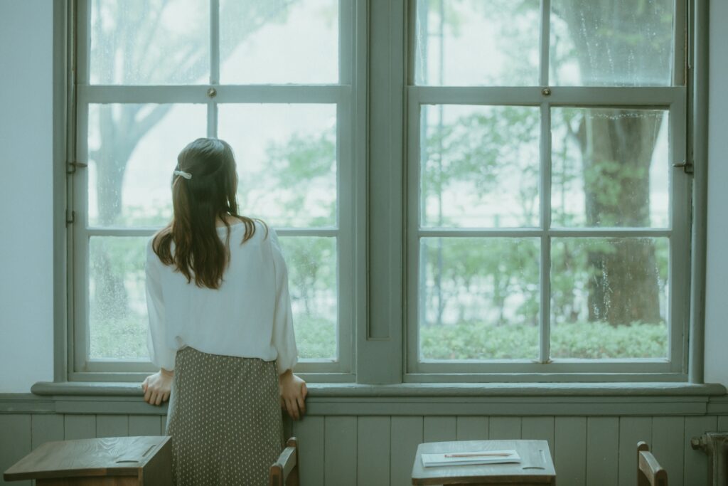 窓の前で外を眺めながら仕事について考える40代の女性の後ろ姿